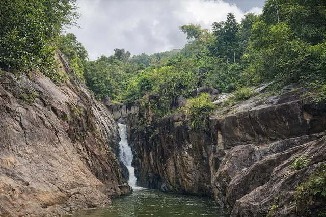 Hidden waterfall at Charco El Hippie dropping into a deep natural pool in the jungle canyon