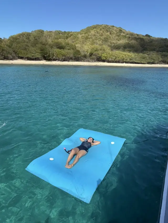 Guest relaxing on a floating mat in clear turquoise water beside an uninhabited island