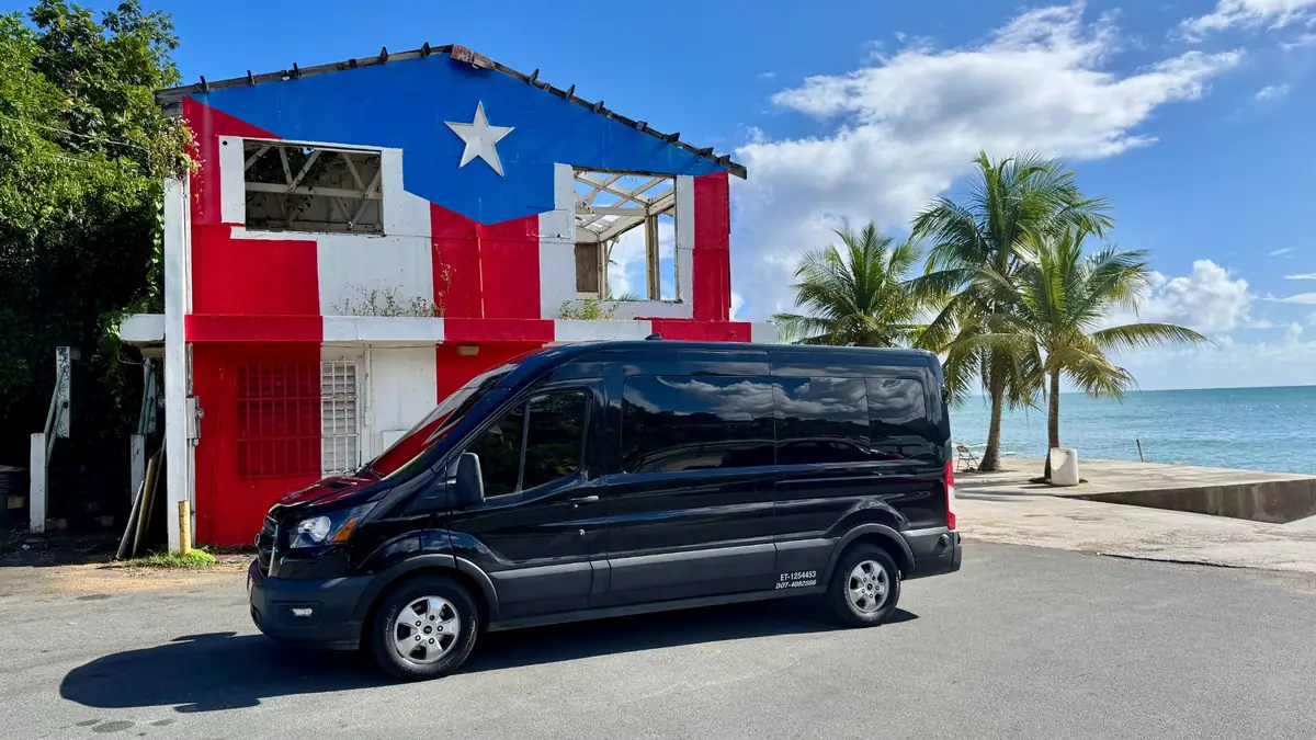 Paradise Seekers Puerto Rico van parked oceanside in front of a building painted with the Puerto Rican flag